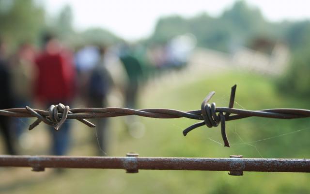 Barbed wire with blurred shapes of migrants