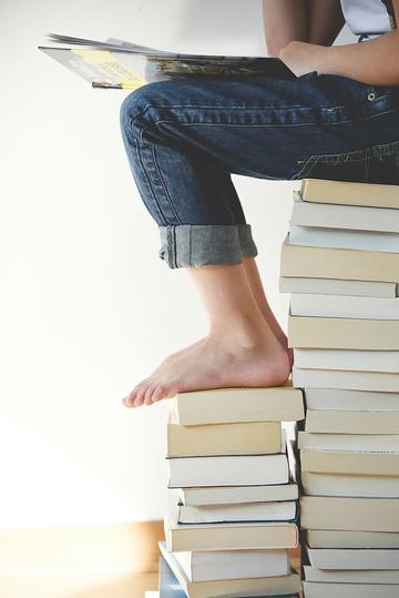 Picture of the lower body of a young person sitting on a stack of books while reading