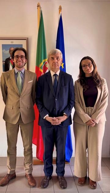 The student with two colleagues of hers in front of the Portuguese and European flags