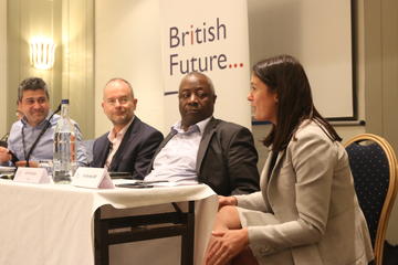 Photograph of discussing in one of British Future's events, in front of the organisation's logo. The panelists are of different genders and ethnic groups