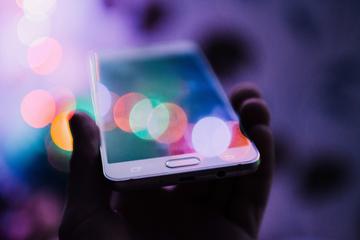 hand holding smartphone with colourful light reflections all over